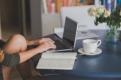 femme devant son ordinateur avec un agenda et son café