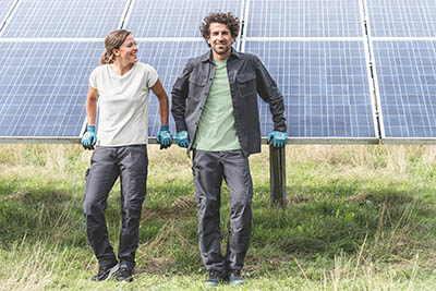 un homme et une femme en tenue de travail contre un panneau solaire